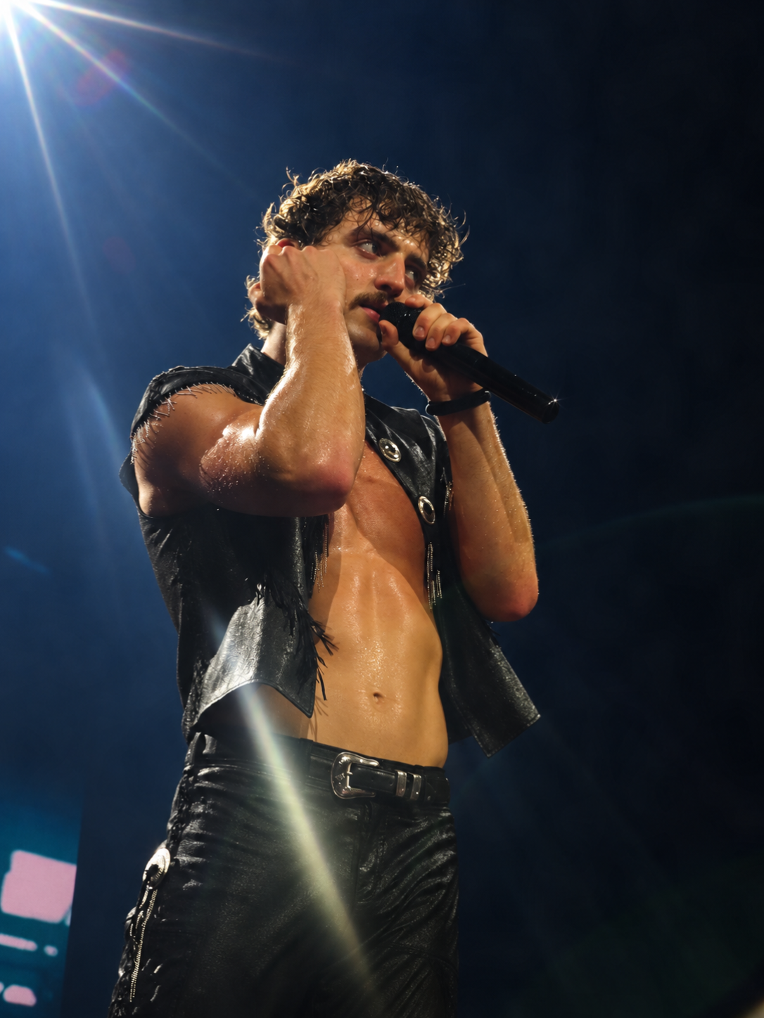 Singer performing with a microphone beneath a bright spotlight